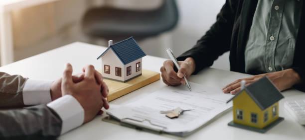 Image of a lady signing a mortgage with two small toy houses next to the contract