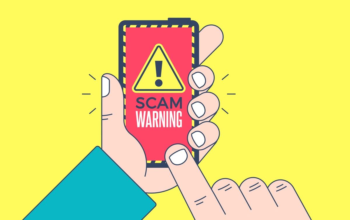 An illustration of a hand holding a phone which has a yellow warning sign with the words 'scam warning' on a red background.