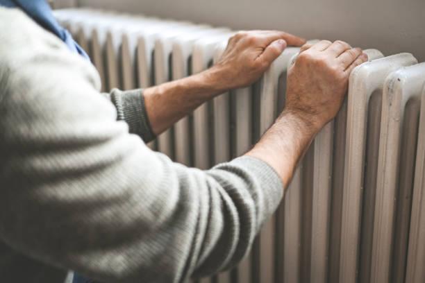 Image of someone warming their hands on a radiator. Energy bills are set to rise again from October. Find out what support is available if you're in energy debt or worried about how you'll heat your home this winter