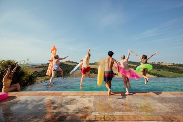 Image of a group of friends jumping into a swimming pool with floaties. Money tops the reason for friendship fall outs on holiday. Six ways to spend-proof your friendships on holiday so everyone returns with happy memories and not debt and regret