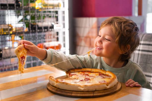 Image of a kid eating a pizza in a restaurant. All the cafes and restaurants where kids can eat for free or £1 during the school summer holidays 2024
