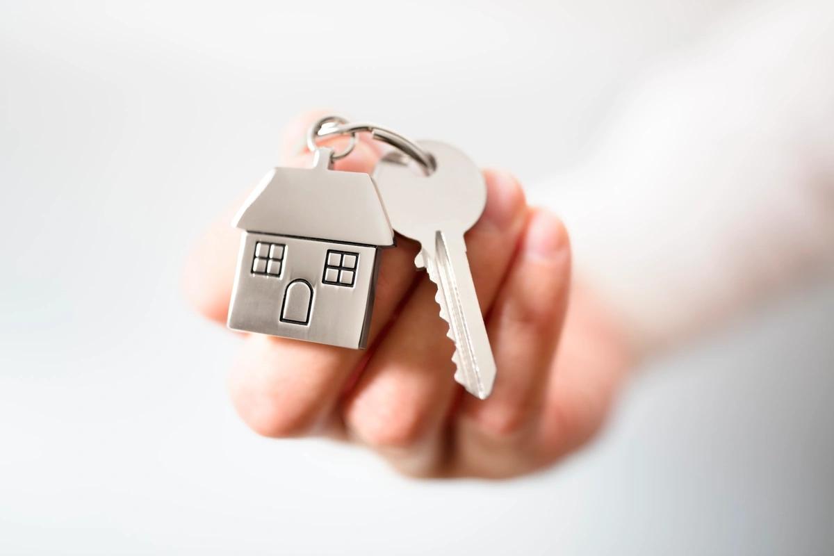 A hand holds out a silver key with a silver house keyring.