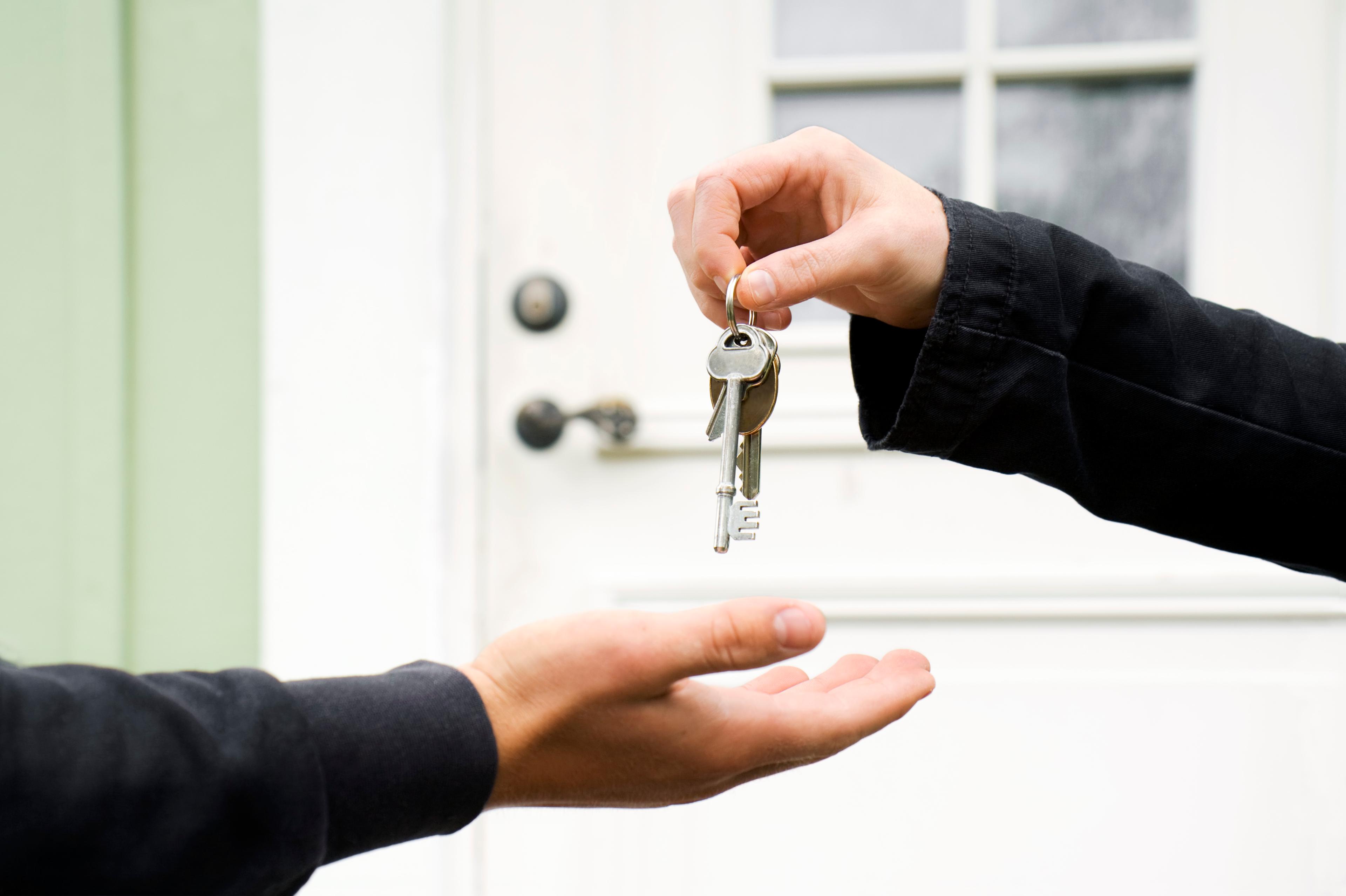 A set of keys exchanging hands outside a house.