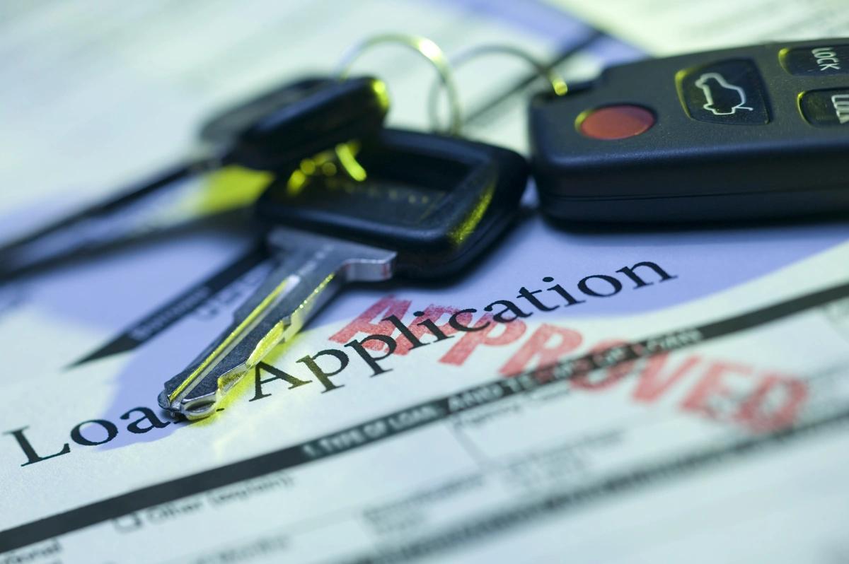 A stock image of car keys on top of an approved loan application.